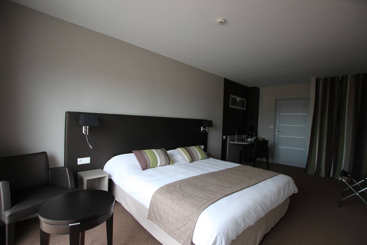 A hotel room with a large bed, a desk, a chair, and a small table.