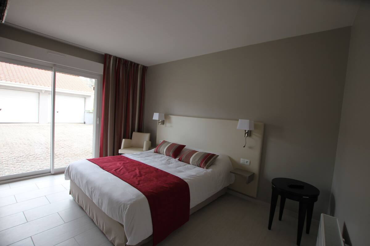A hotel room with a large bed, a chair, a small table, and a sliding glass door leading to a courtyard.