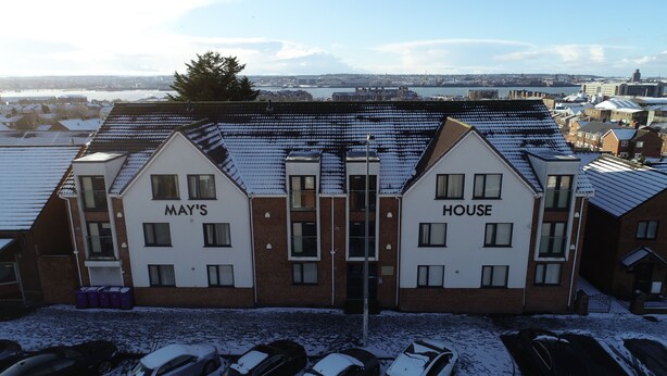 A building with two sections labeled "MAY'S" and "HOUSE" with a view of a snowy landscape and a river in the background. - May's House (Liverpool)