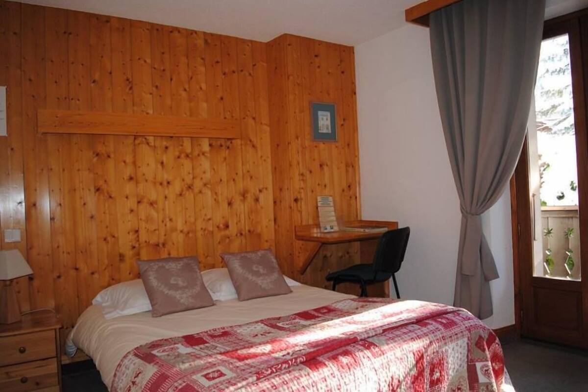 Une pièce aux murs lambrés, avec un lit, un bureau et une chaise.