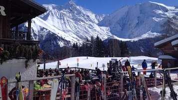 A ski lodge with a wooden exterior, a covered seating area, and a view of snow-covered mountains.