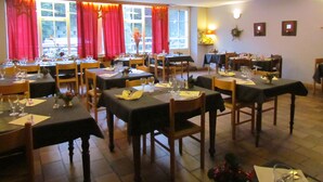 A dining area with tables set for service, large windows with red curtains, and a warm interior lighting. - Hôtel Val Joly (Saint-Gervais-les-Bains)