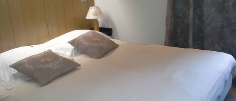 A neatly made bed with two pillows, a wooden headboard, a bedside lamp, and a curtain with a floral pattern.