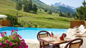 Een zwembadterras met een eettafel, met uitzicht op een bergachtig landschap.