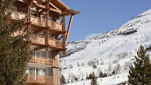 Een houten chalet met balkons, een piste op de achtergrond en een heldere lucht.