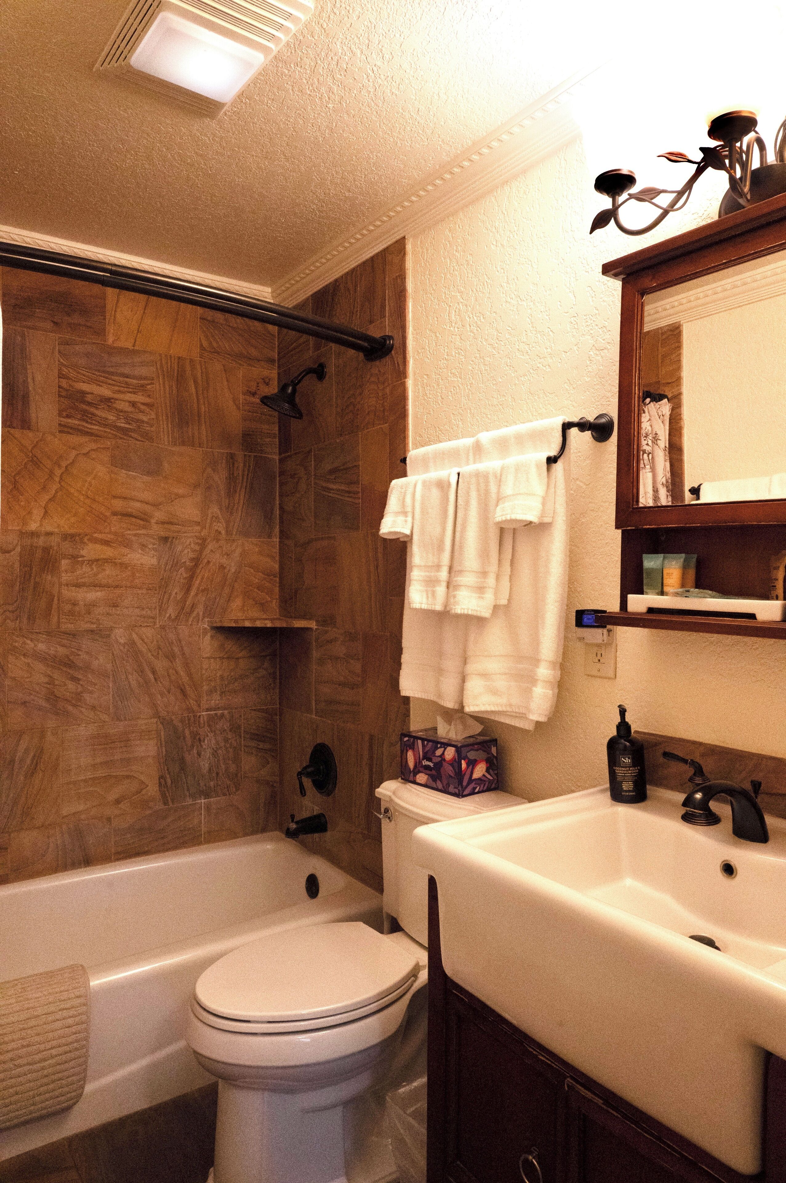 Une salle de bain avec une cabine de douche en bois, des toilettes blanches, une baignoire et un lavabo avec un miroir au-dessus.