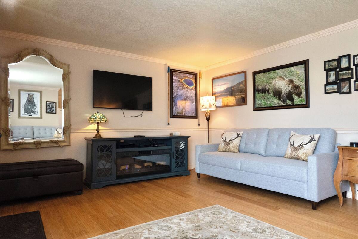 A living room with a light blue sofa, a dark entertainment unit, a flat-screen TV, and framed pictures on the wall.