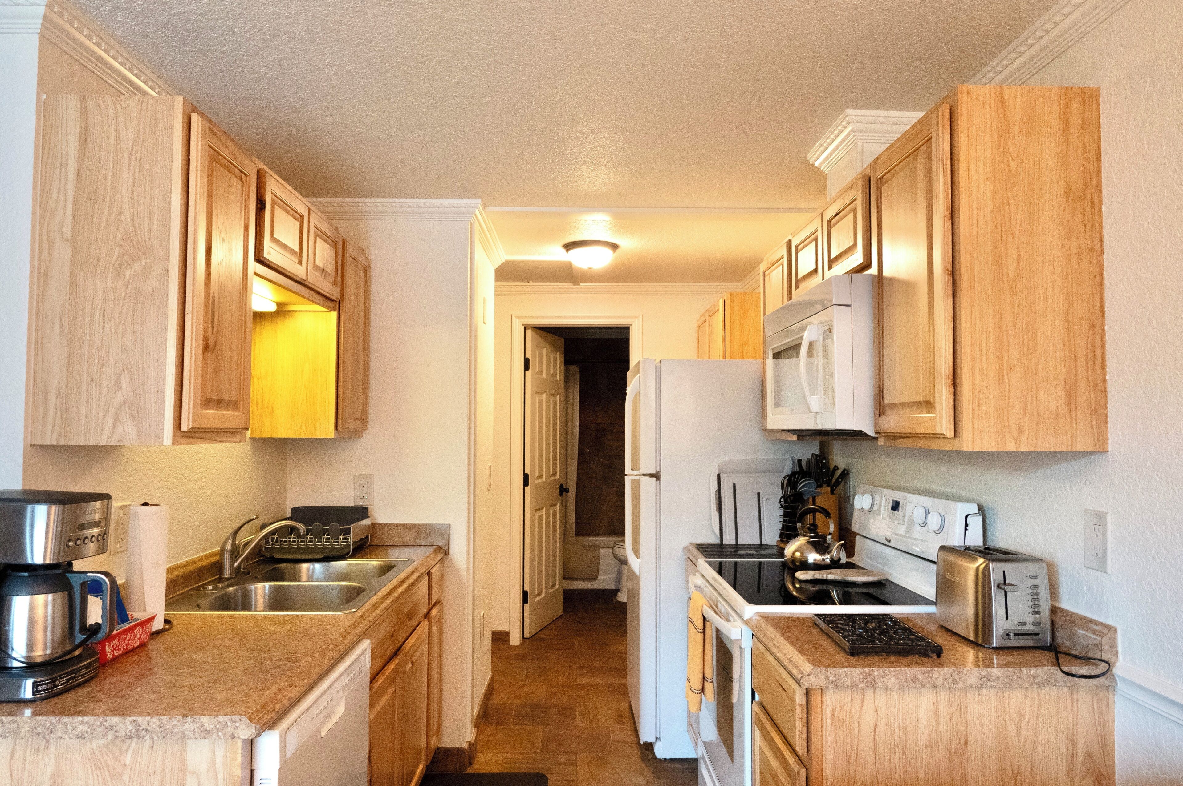 A compact kitchen with wooden cabinets, a stainless steel sink, a built-in oven, and a microwave.