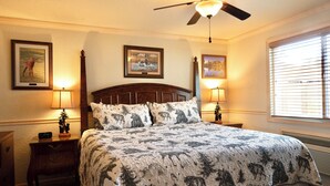 A bedroom with a large bed, two bedside tables with lamps, a ceiling fan, and framed pictures on the walls. - Yellowstone Gateway Inn (Gardiner)
