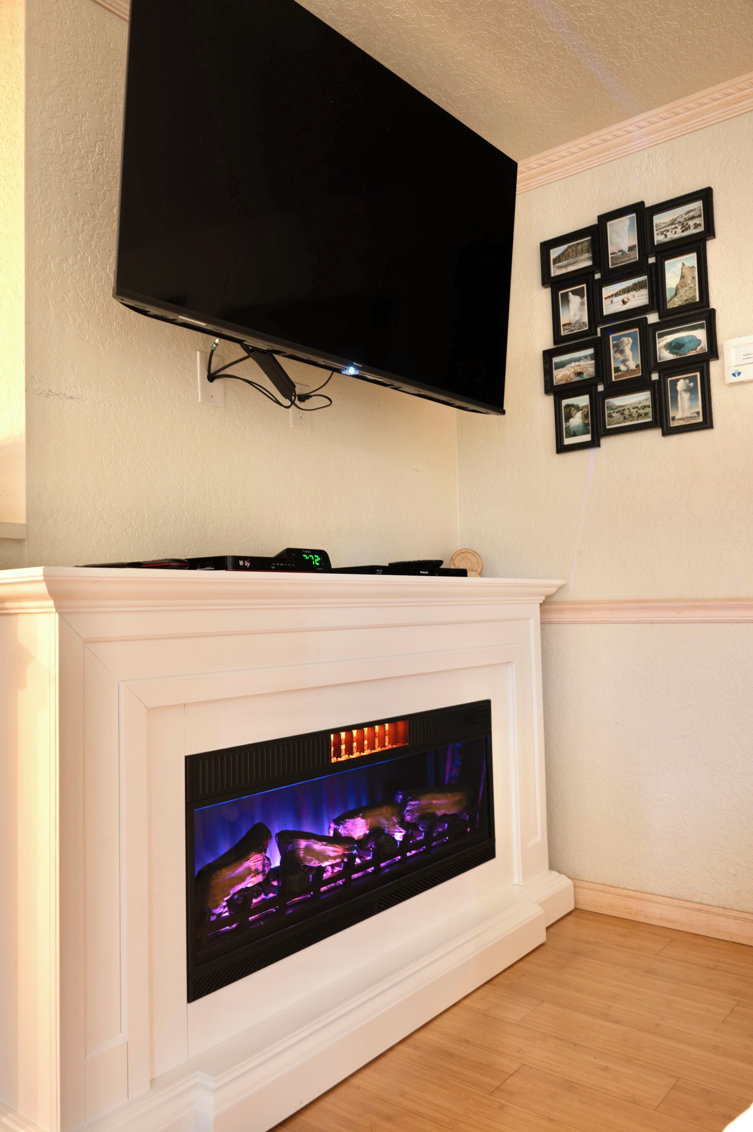 A fireplace with a TV mounted above it, a wall-mounted clock, and a series of framed pictures.