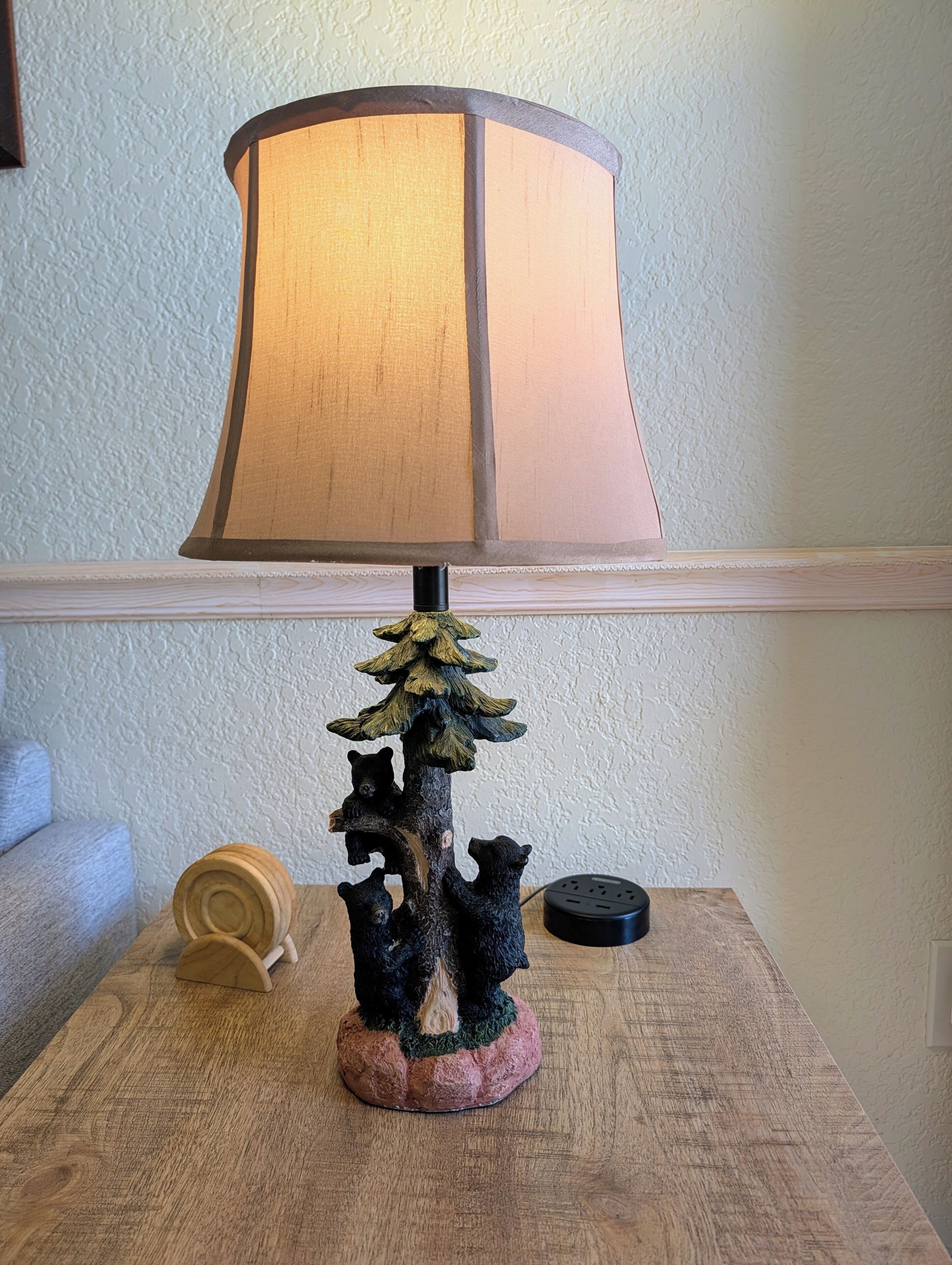 A table lamp with a wooden base and a tree design, placed on a wooden table.