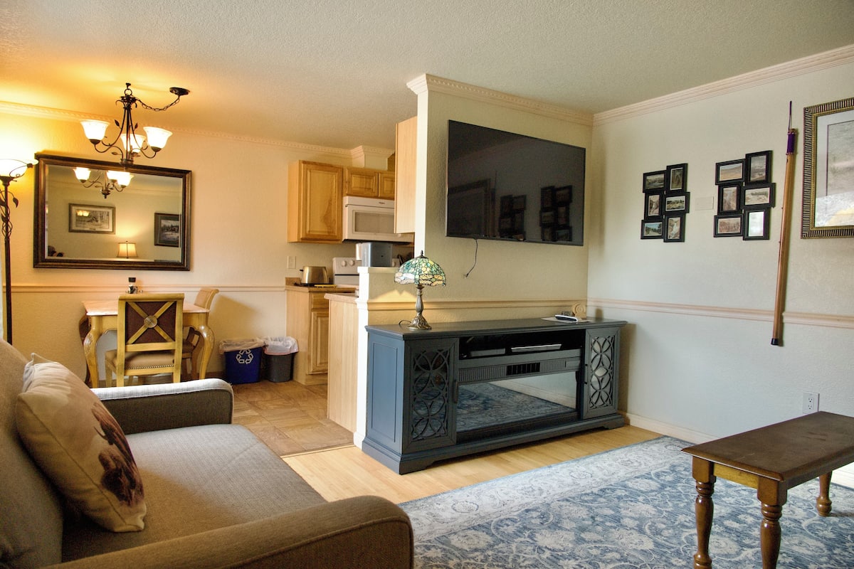 A living room with a sofa, a coffee table, a TV stand, and a dining area with a table and chairs.
