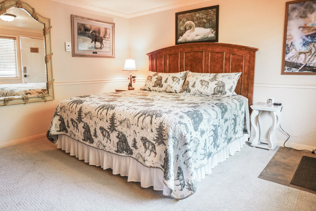 A bedroom with a large bed, a wooden headboard, a mirror, and a framed picture on the wall.
