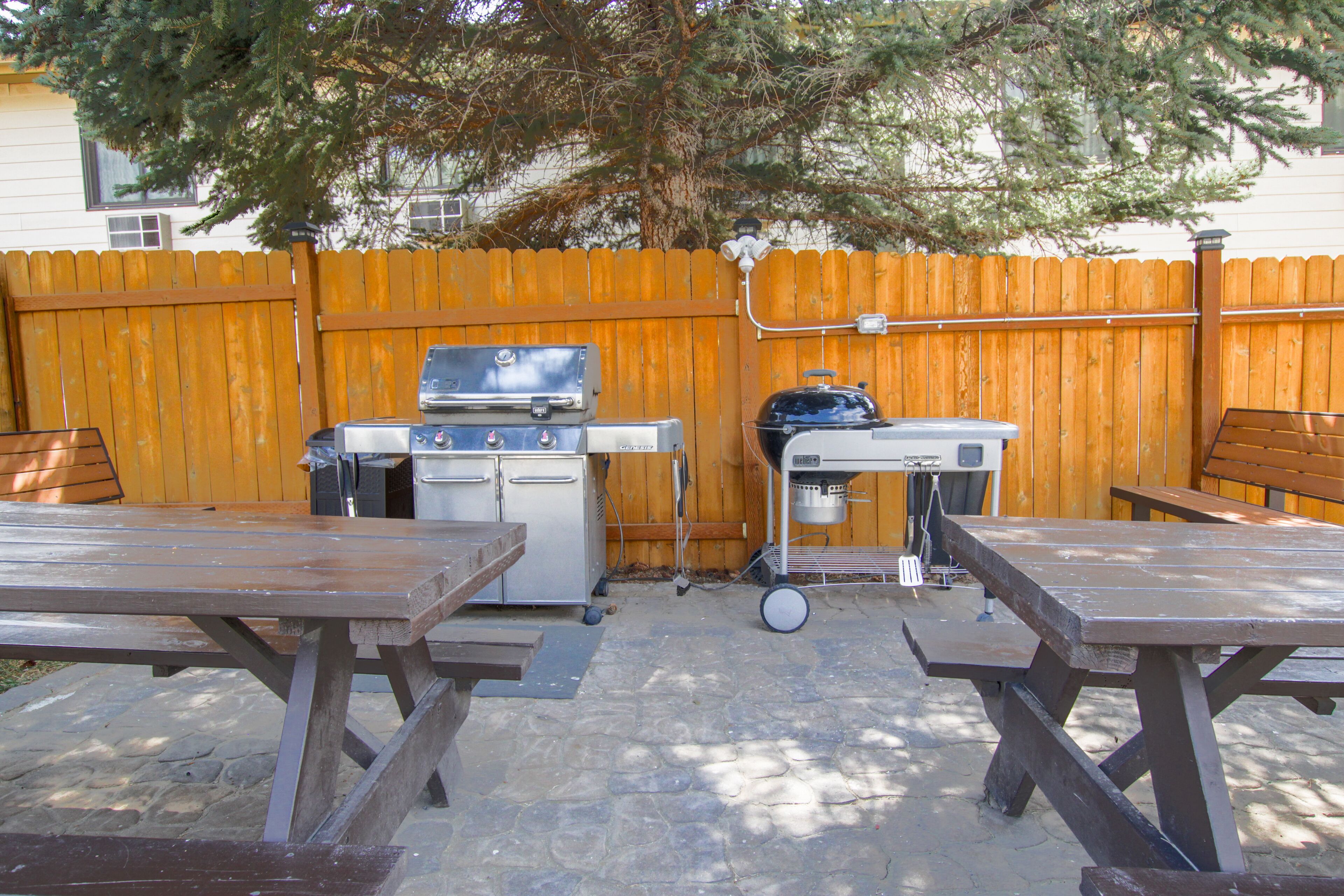 An outdoor patio with picnic tables, a barbecue grill, and a grill cart.