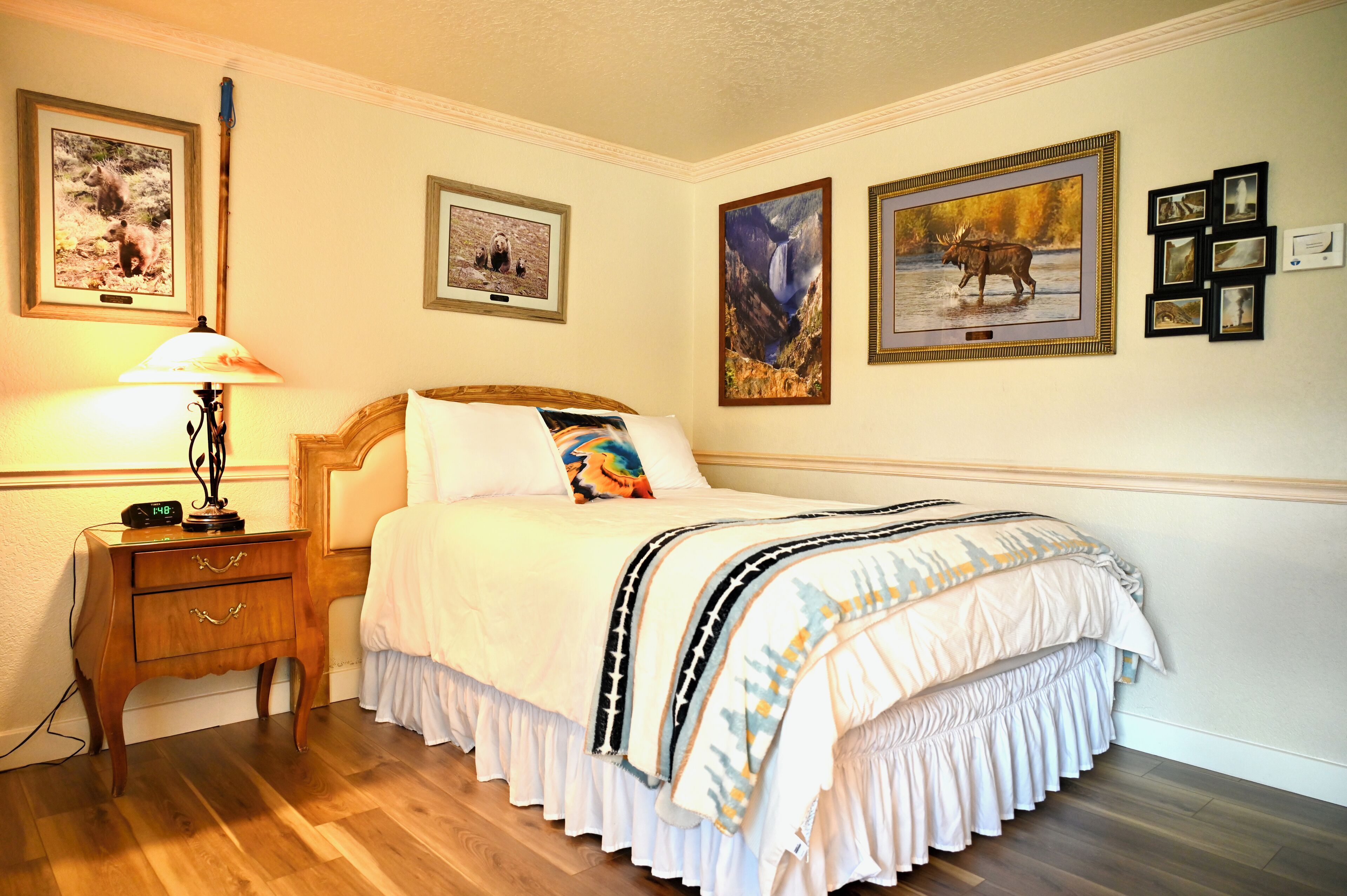 A neatly arranged bedroom with a wooden nightstand, a bed with a white and patterned bedspread, and framed wildlife pictures on the wall.