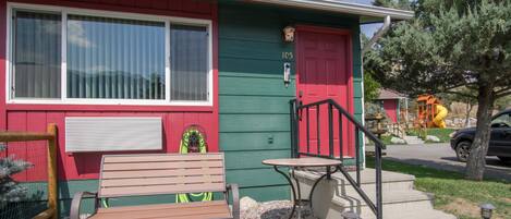 A house with a red door, a green exterior, and a bench outside.