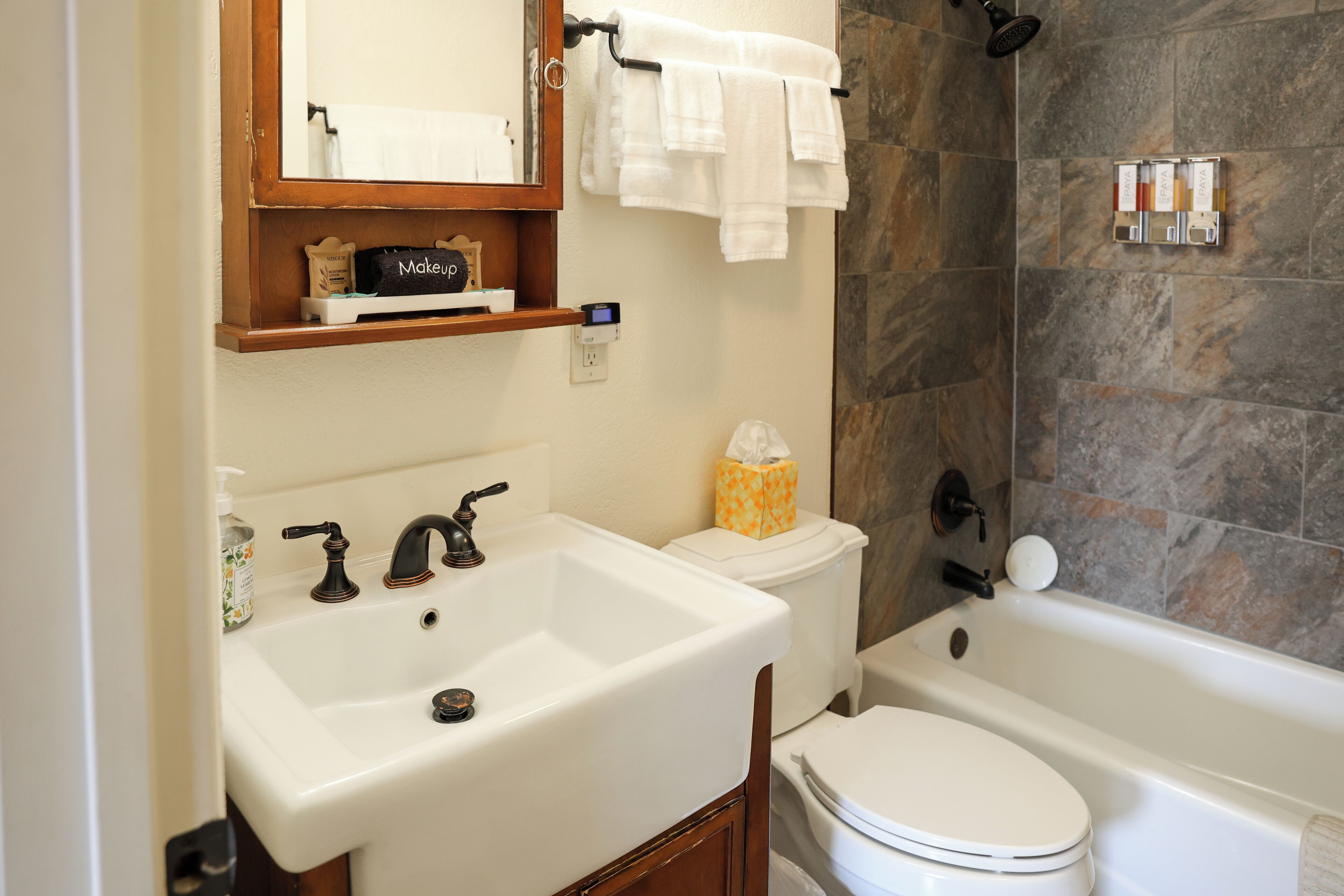 Un baño con un lavabo blanco, un inodoro y una bañera. Hay un espejo sobre el lavabo y un perchero encima de la bañera.