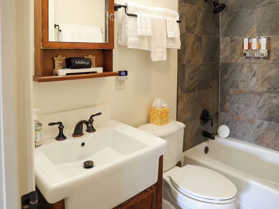Un baño con un lavabo blanco, un inodoro y una bañera. Hay un espejo sobre el lavabo y un perchero encima de la bañera.
