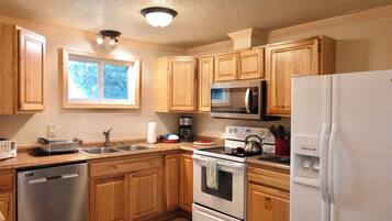 Una cocina con armarios de madera, electrodomésticos de acero inoxidable, lavavajillas y una ventana que proporciona luz natural.