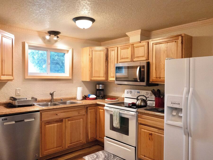 Una cocina con armarios de madera, electrodomésticos de acero inoxidable, lavavajillas y una ventana que proporciona luz natural.