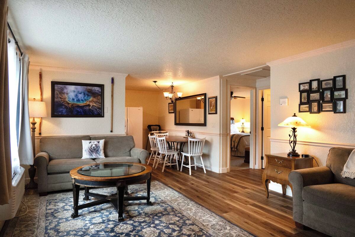 A living room with a sofa, a coffee table, a dining table with chairs, and a lamp.