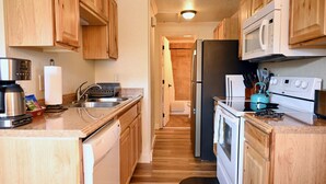 A compact kitchen with wooden cabinets, a stainless steel sink, a microwave, a stove, and a refrigerator. - Yellowstone Gateway Inn (Gardiner)