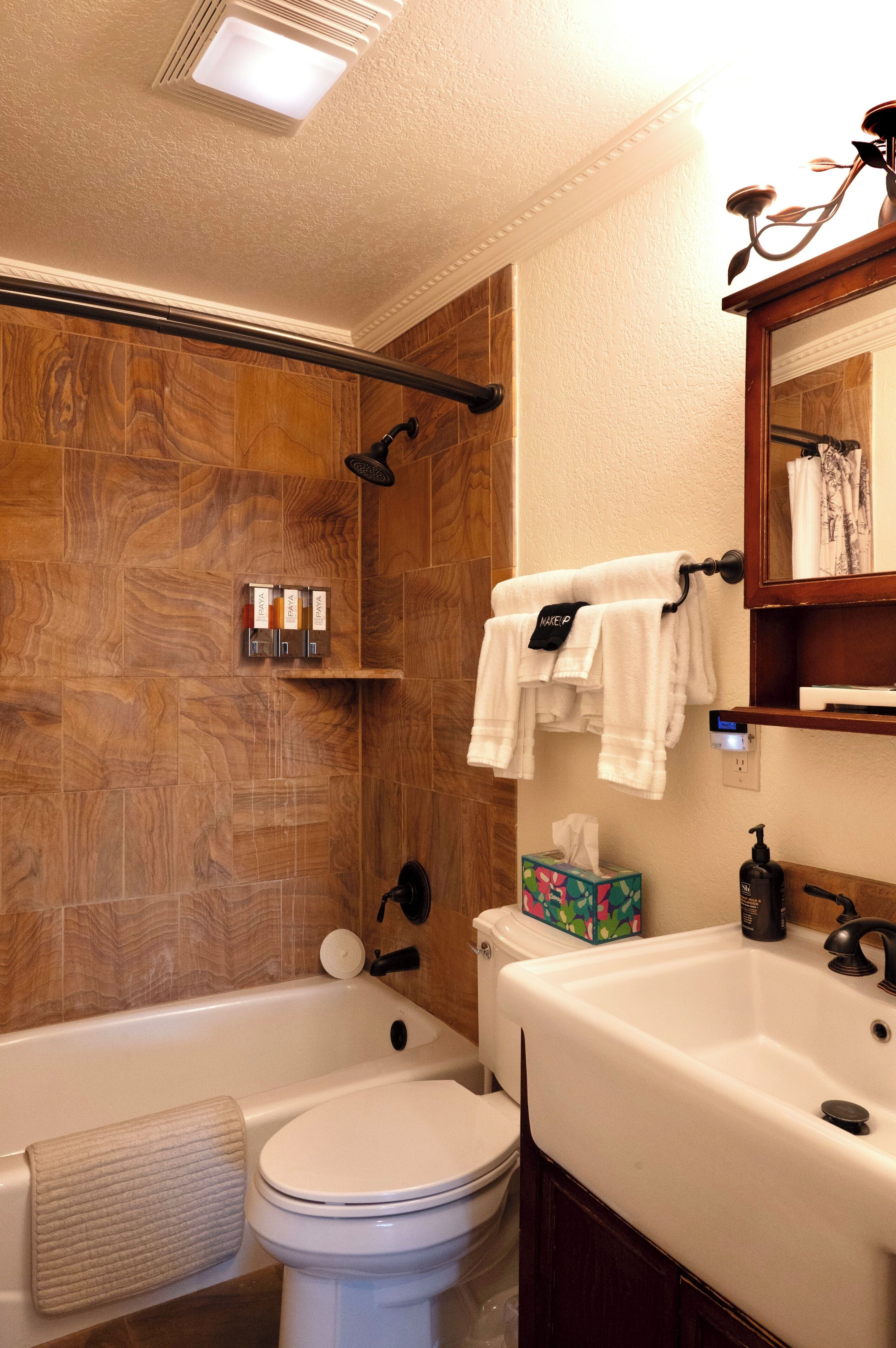 Une salle de bain avec un mur en bois, une baignoire, des toilettes, un lavabo et un miroir.