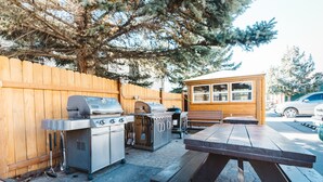 An outdoor patio with a barbecue grill, a grill cart, and a wooden fence. - Yellowstone Gateway Inn (Gardiner)
