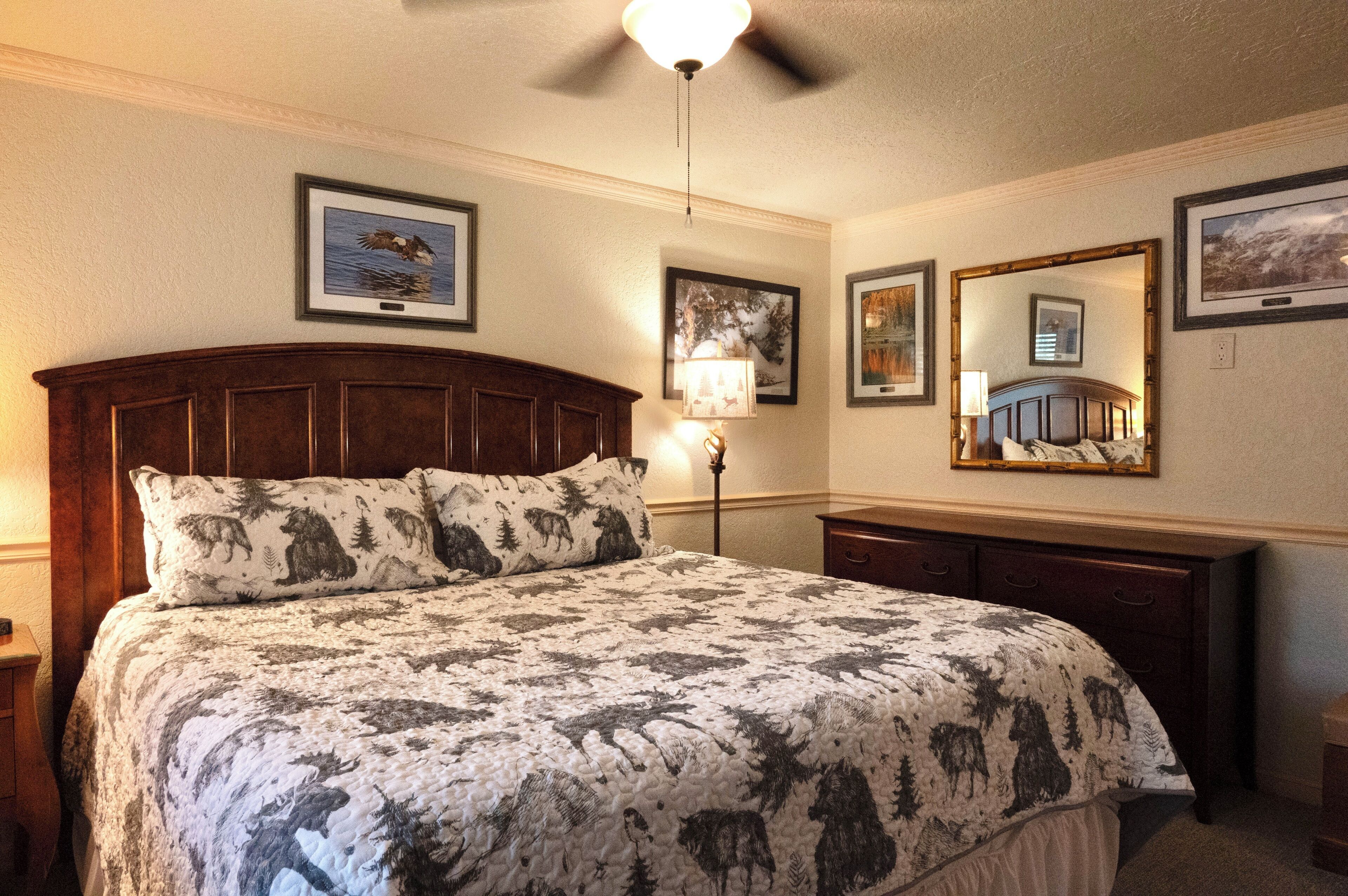 A bedroom with a large bed, a wooden headboard, a nightstand, a lamp, and framed pictures on the walls.