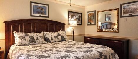 A bedroom with a large bed, a wooden headboard, a nightstand, a lamp, and framed pictures on the walls.