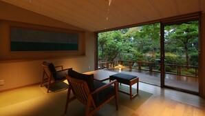 A modern interior with a wooden dining table, chairs, and a large sliding glass door leading to a balcony with a view of trees. - Monjusou (Miyazu)