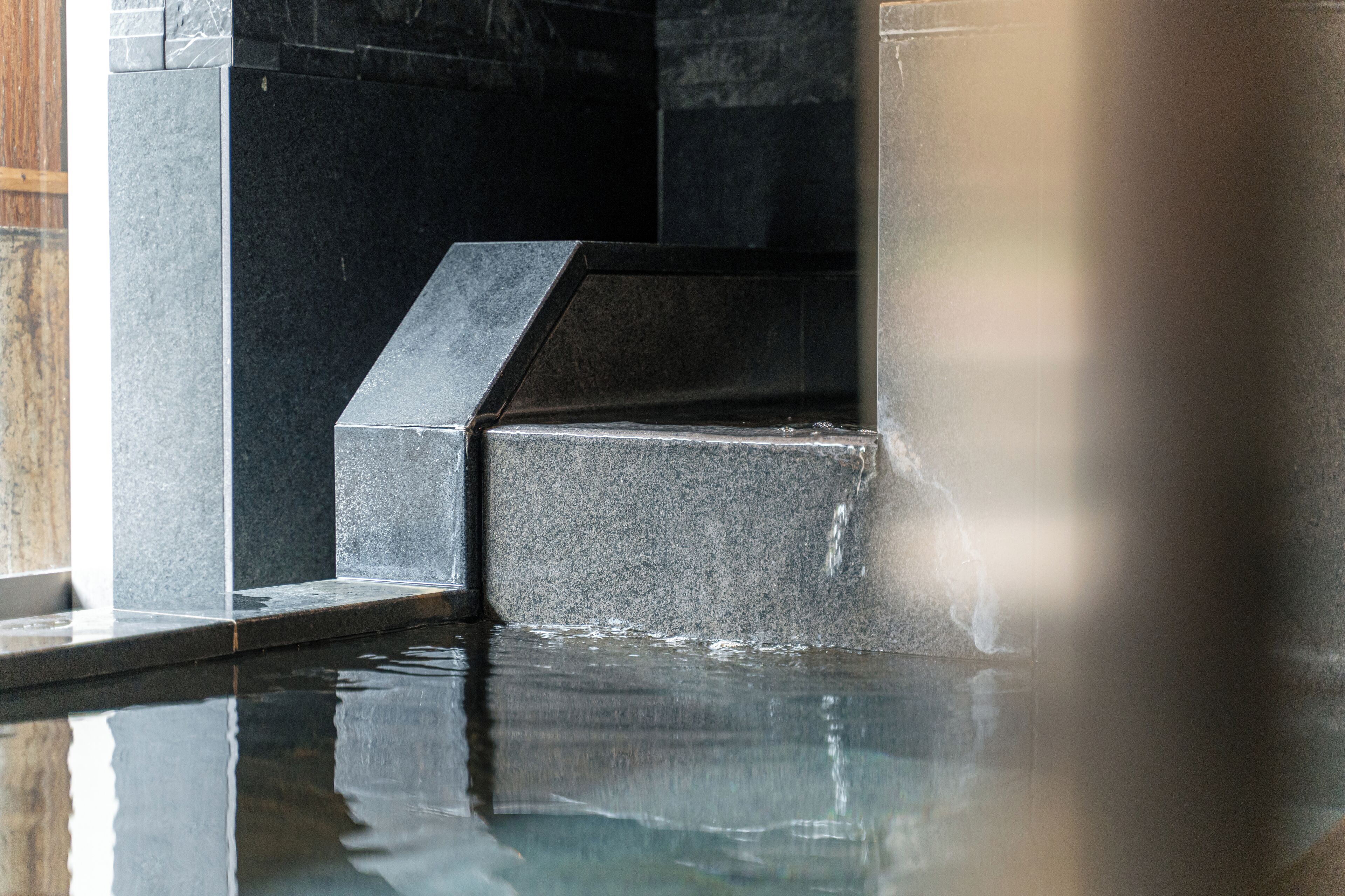 Área de piscina com degraus de pedra e superfície aquática reflexiva.