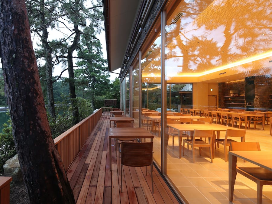 A wooden deck with tables and chairs, overlooking a body of water and trees.