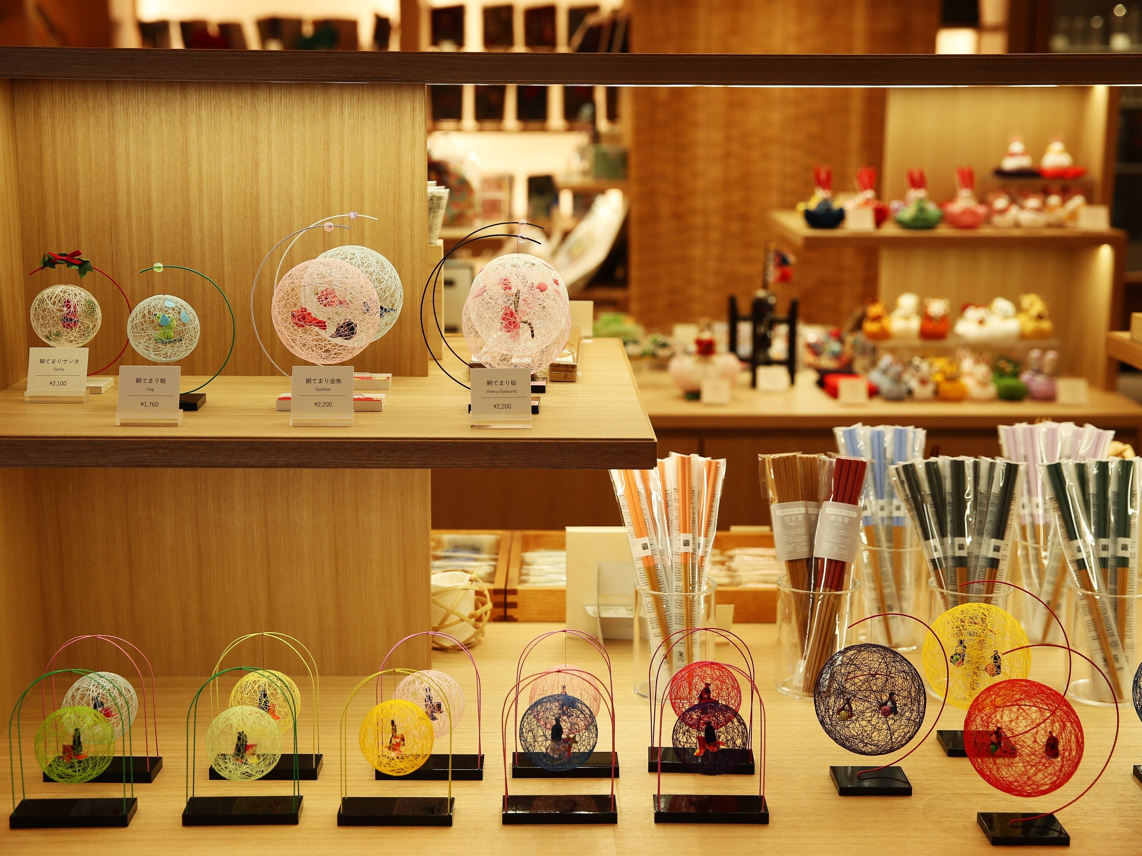 Una exhibición de esferas de vidrio decorativas con figuras en su interior, con precios desde ¥1,760 hasta ¥2,200, y una variedad de otros artículos en estantes de una tienda.