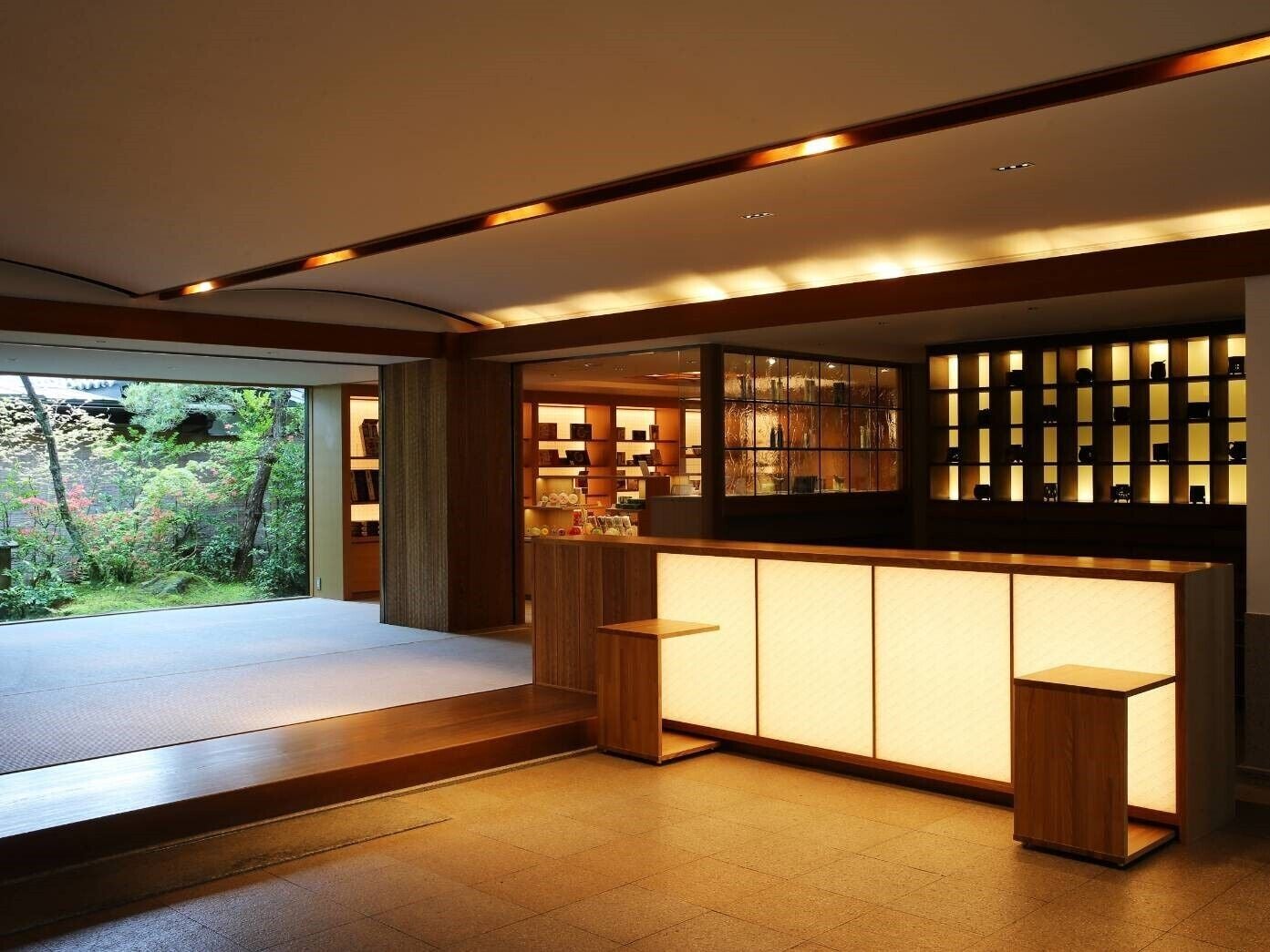 A modern interior with a reception desk, wooden flooring, and a view of greenery outside.