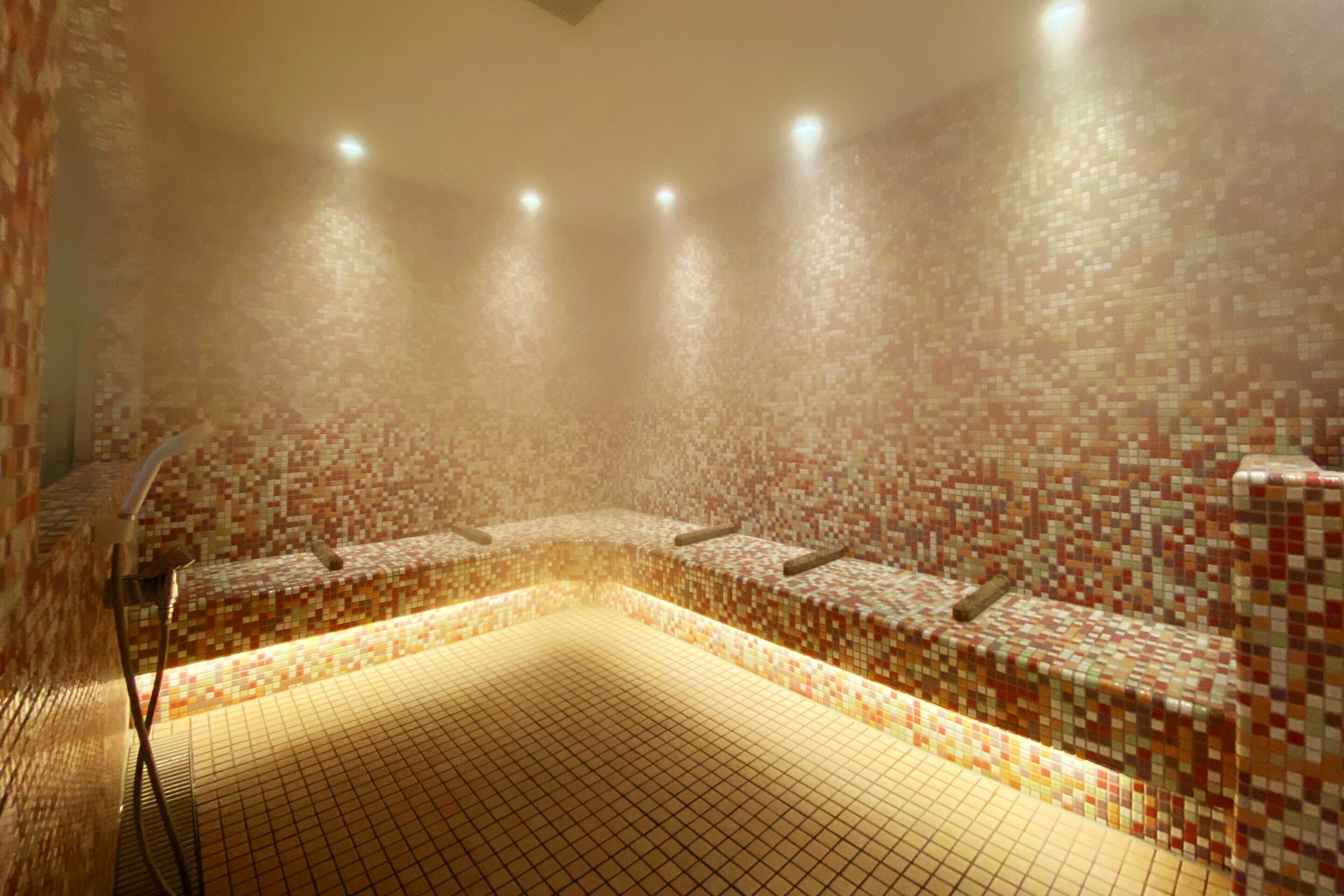 A tiled room with a central seating area and a shower.