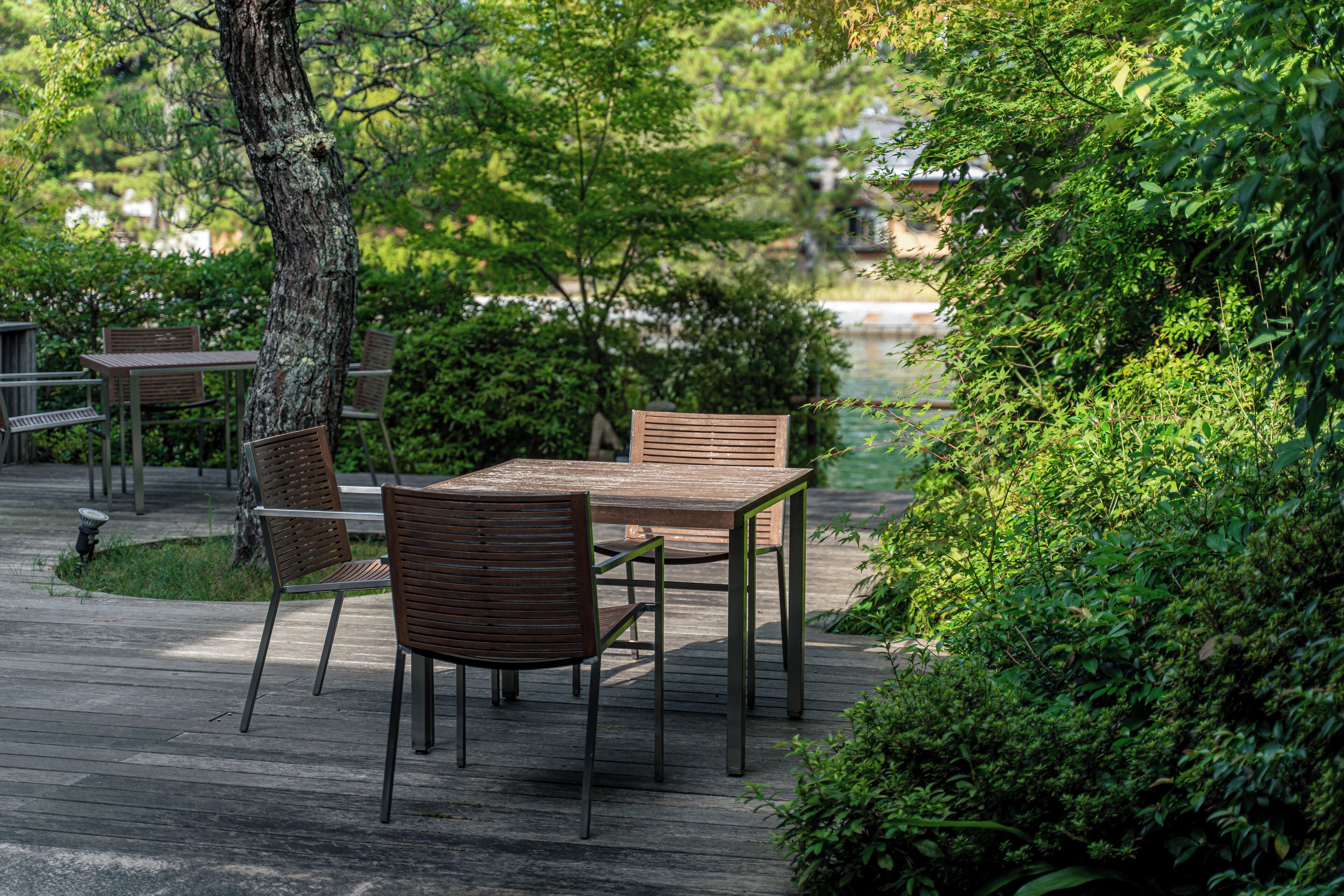 Eine Holzterrasse mit Tisch und Stühlen, umgeben von üppigem Grün und einem Baum.
