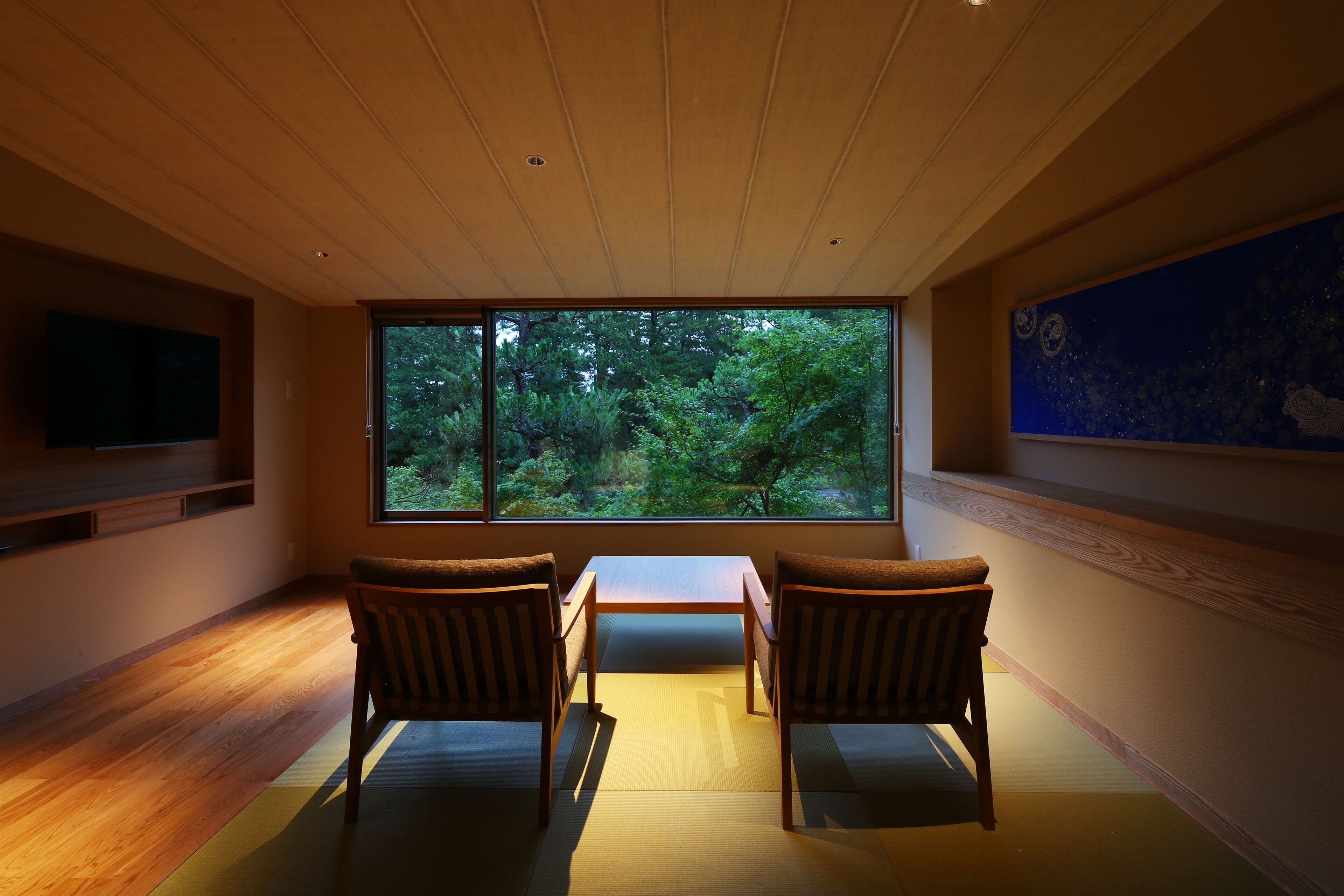 A room with a large window, wooden floor, tatami mat, and a flat-screen TV.