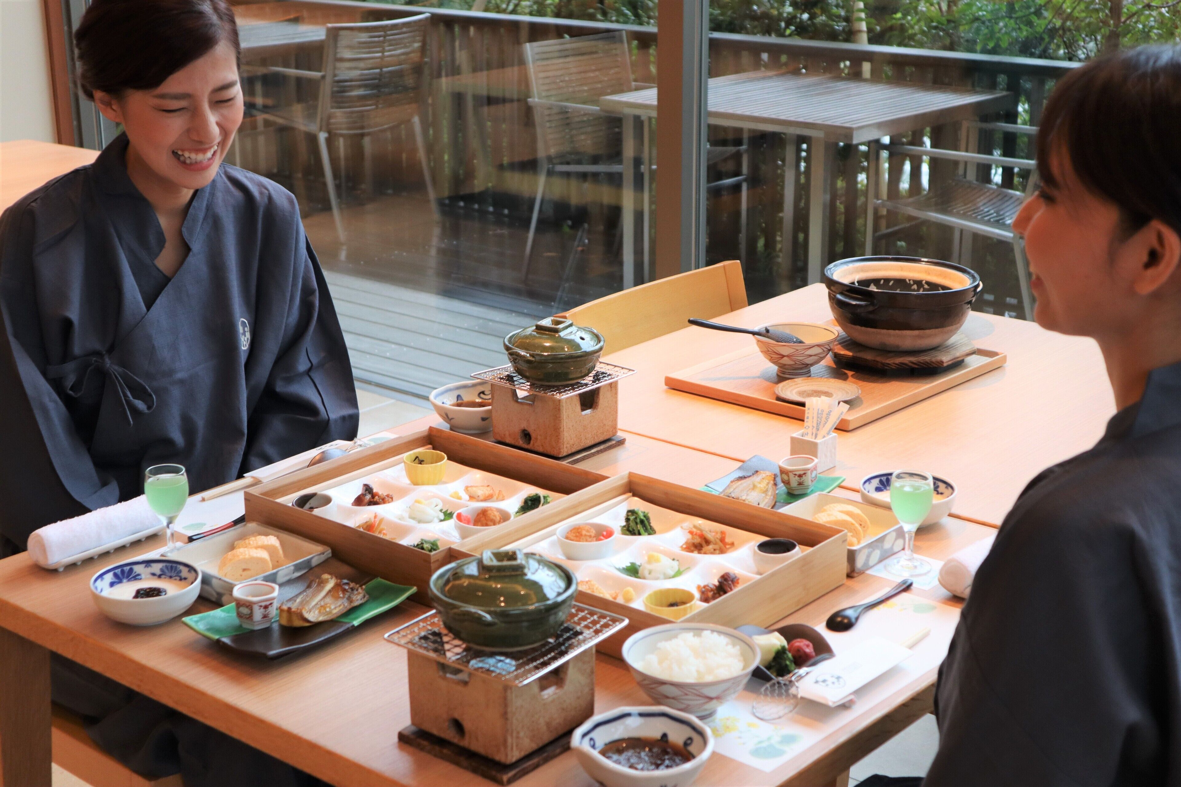 A dining table with various dishes and a teapot, set in a room with a view of a wooden deck and chairs outside.