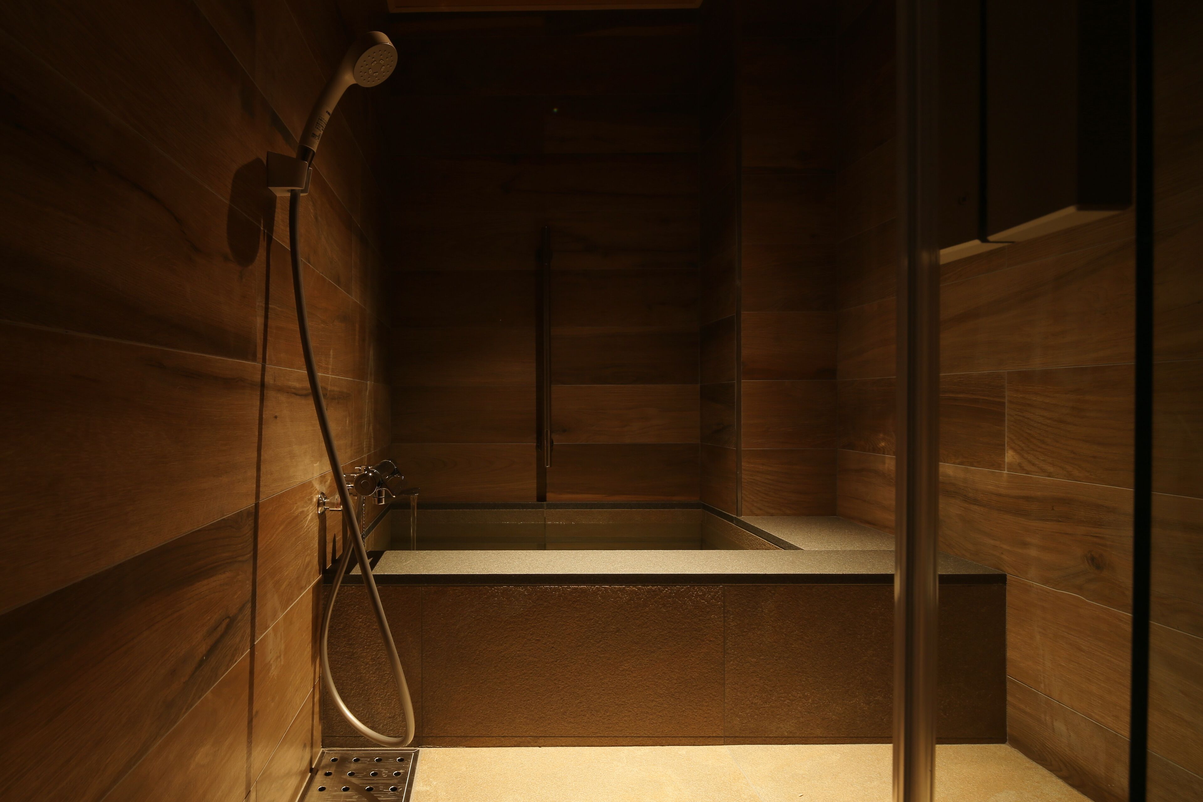 A modern shower with wooden paneling and a glass door.