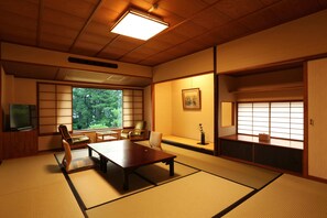 A traditional Japanese room with tatami flooring, a low table, chairs, a television, and sliding doors.