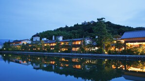 A waterfront hotel with multiple buildings, a reflection in the water, and a hill in the background. - Monjusou (Miyazu)