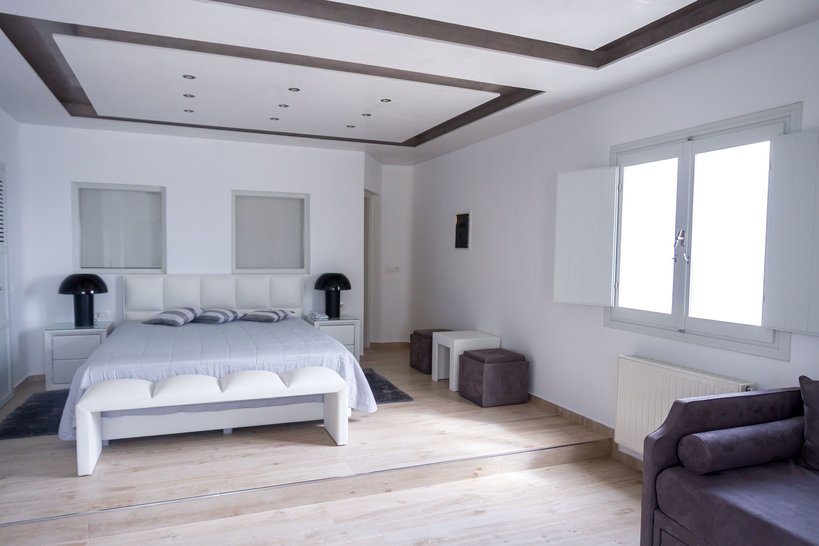Un dormitorio moderno con una cama grande, mesitas de noche, una ventana y un radiador.
