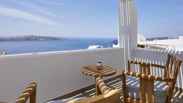 Una silla y una mesa de madera en un balcón con vistas al mar y a islas distantes.
