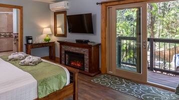 A bedroom with a bed, a fireplace, a television, and a sliding glass door leading to an outdoor deck.