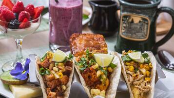 Tre tacos con diversi condimenti, una ciotola di frutti di bosco misti, un frullato e una tazza su un tavolo.