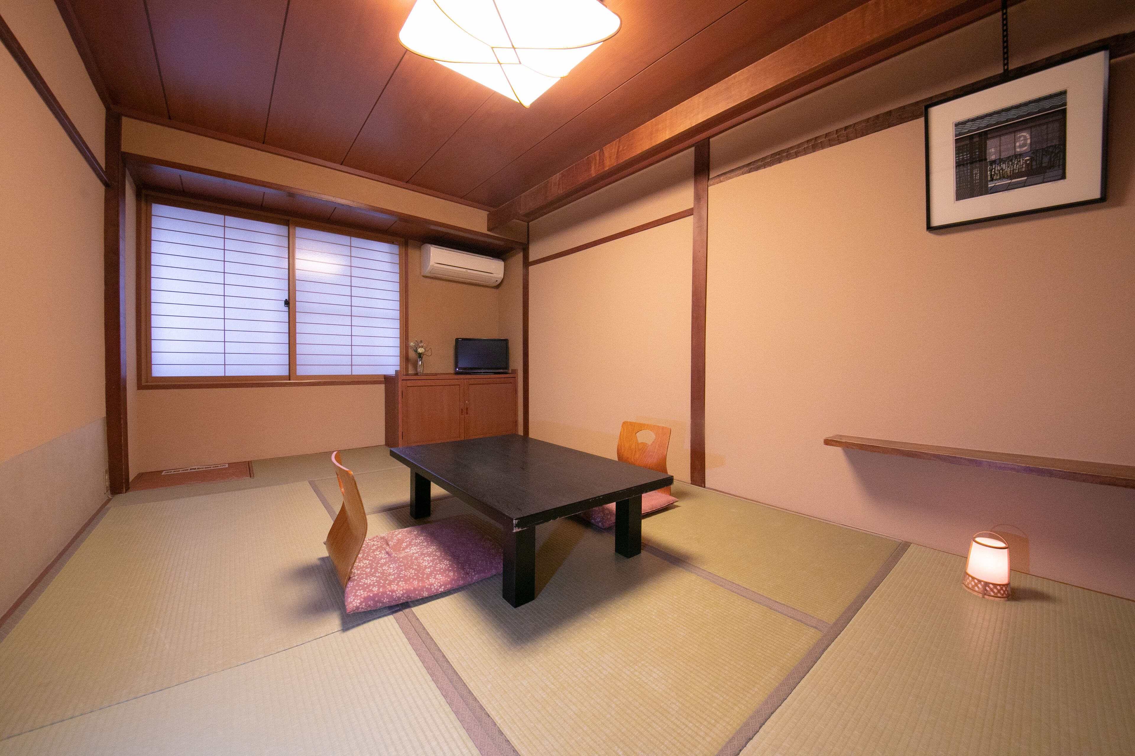 A traditional Japanese room with tatami flooring, a low table, a television, and a small lamp.