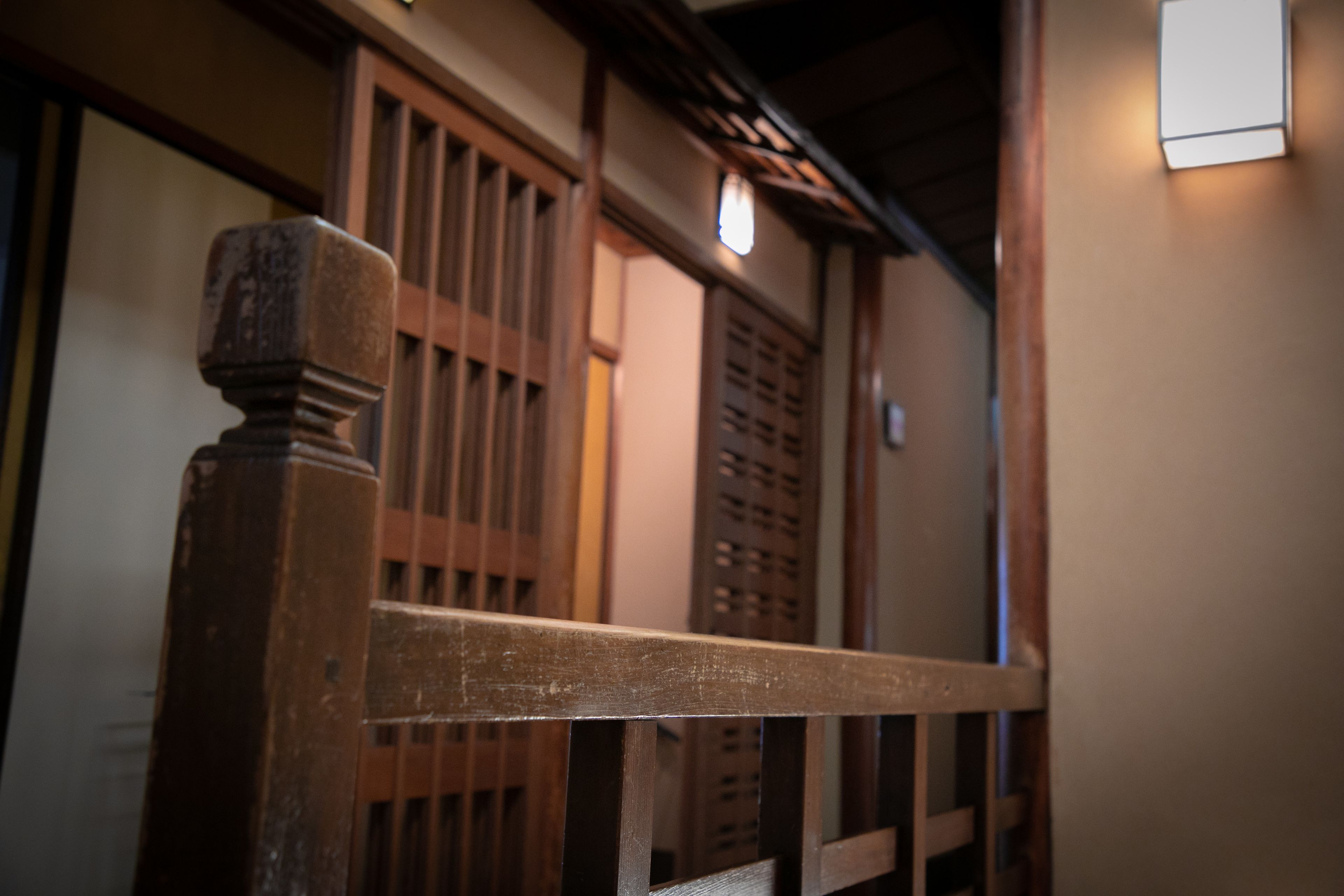 A wooden staircase with a handrail, leading to a room with traditional wooden sliding doors.