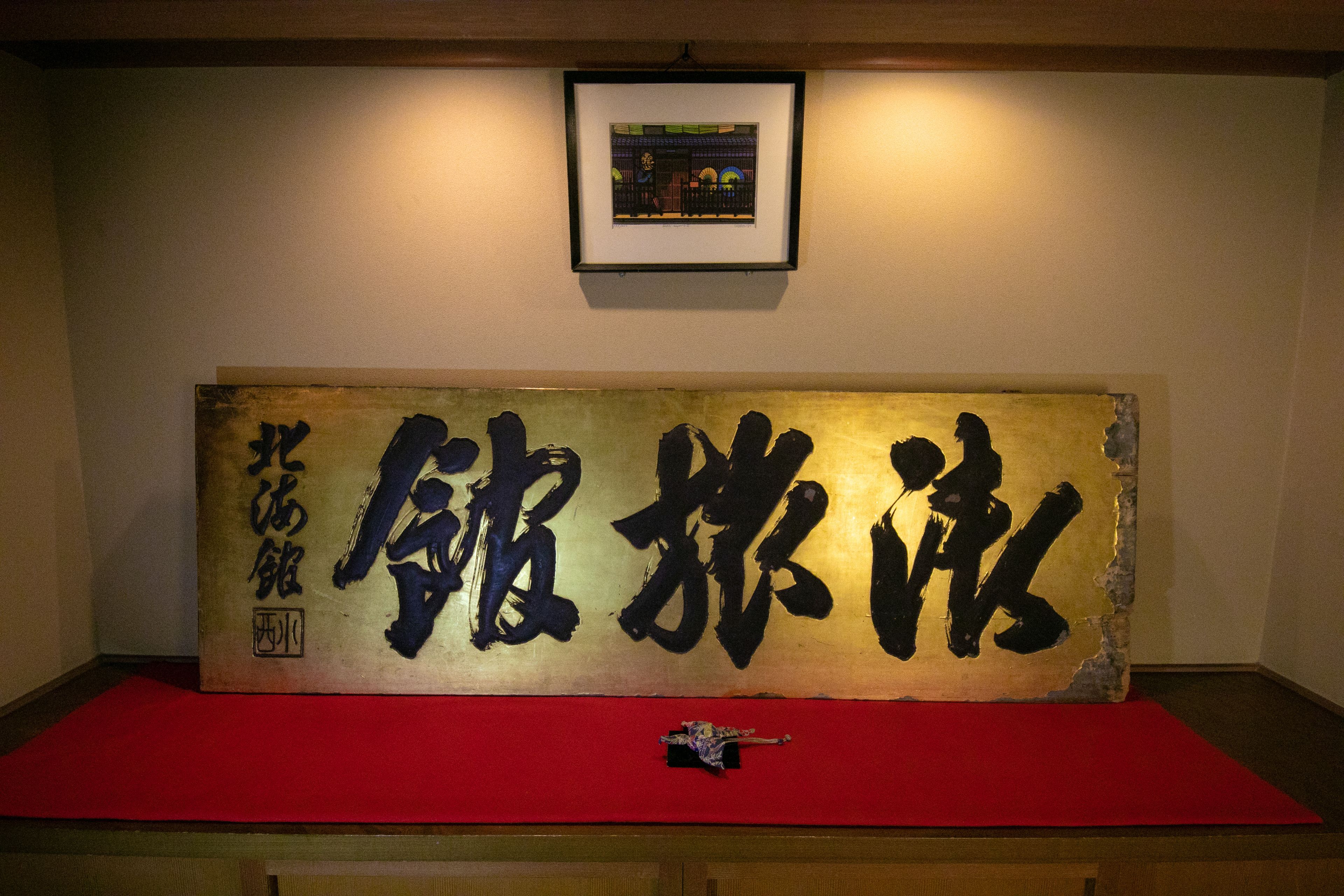 A framed calligraphy artwork on a wall with a red mat below.