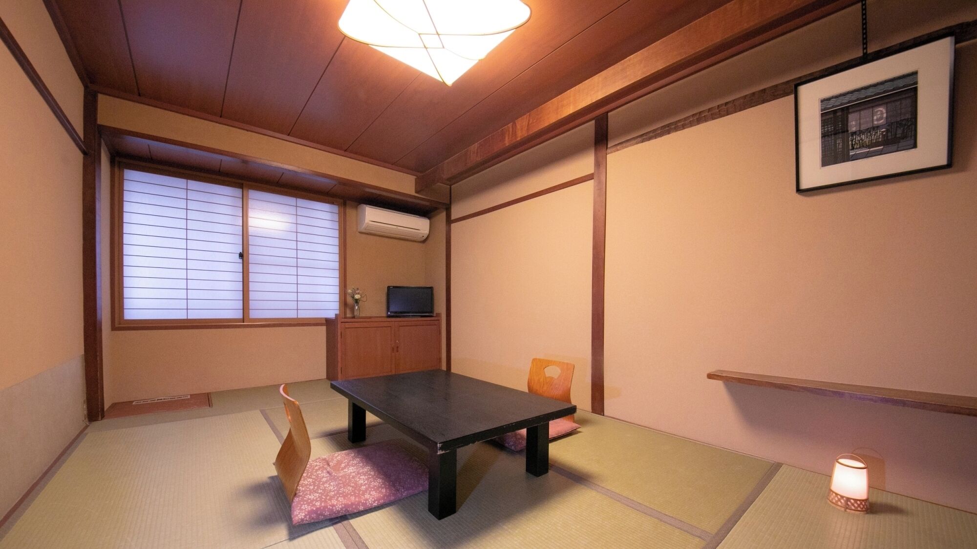 A traditional Japanese room with tatami flooring, a low table, a television, and sliding doors.